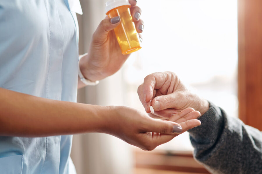 older woman picking a pill out of caretakers hand