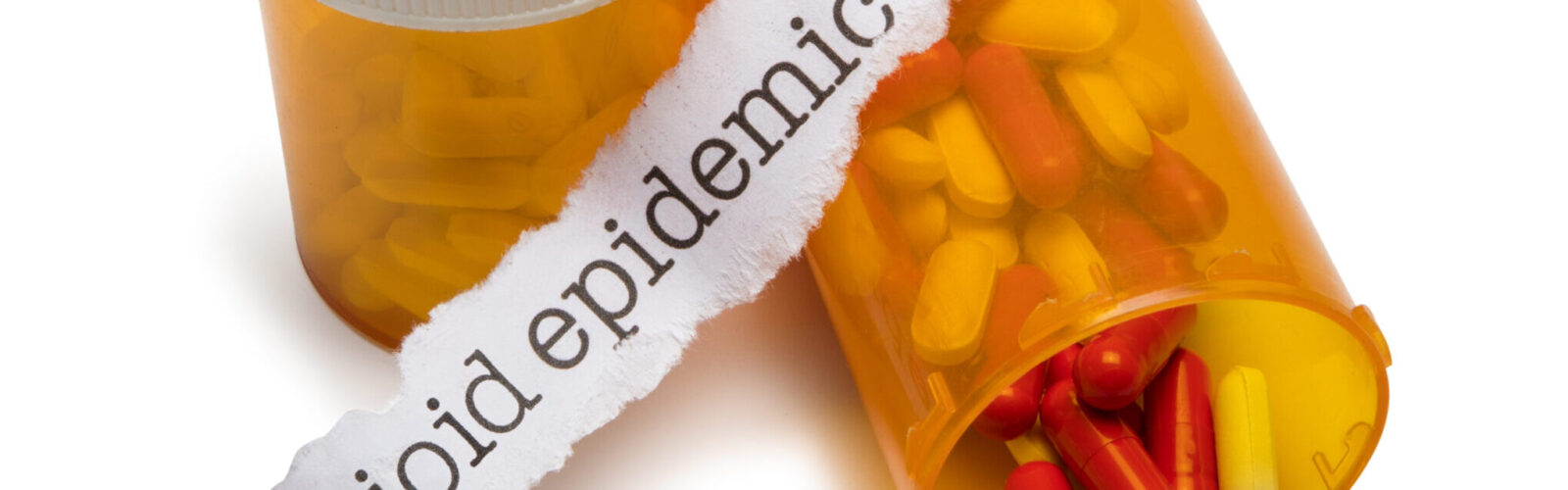 pills and pill bottles with slip of paper with the words opioid epidemic on it