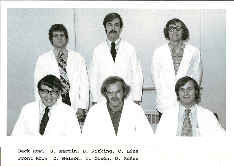 A black-and-white group photo of pharmacy students in white coats.