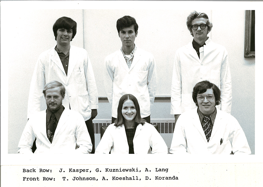 A black-and-white group photo of pharmacy students in white coats.