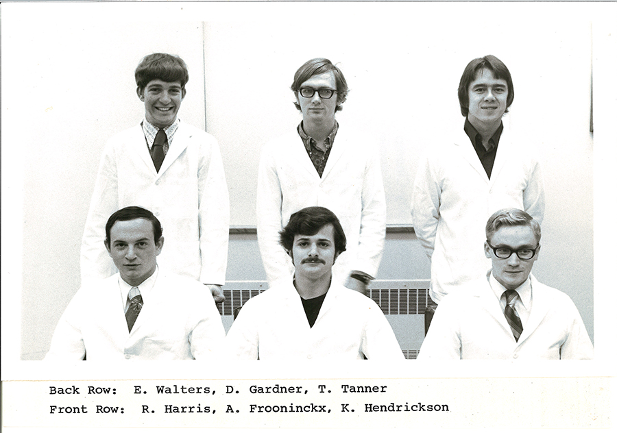 A black-and-white group photo of pharmacy students in white coats.