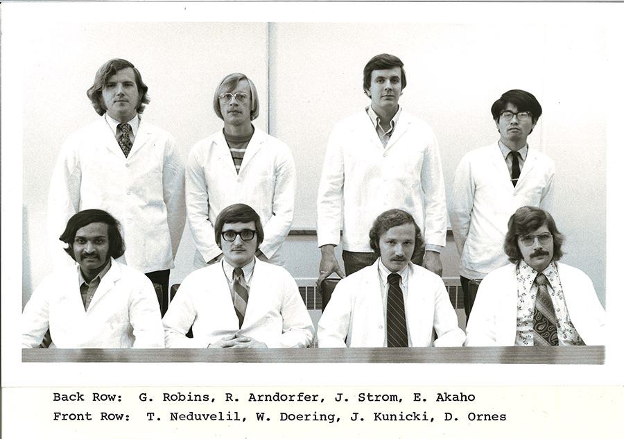 A black-and-white group photo of pharmacy students in white coats.