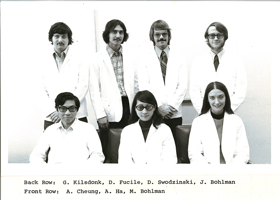 A black-and-white group photo of pharmacy students in white coats.