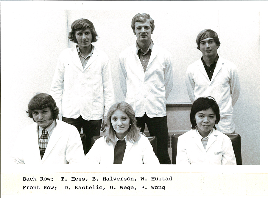 A black-and-white group photo of pharmacy students in white coats.