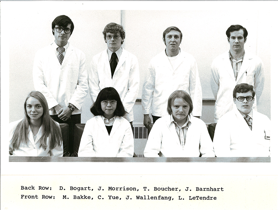 A black-and-white group photo of pharmacy students in white coats.