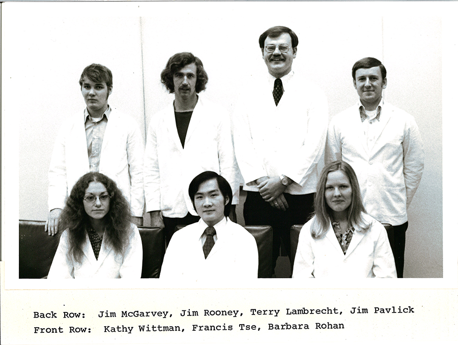 A black-and-white group photo of pharmacy students in white coats.