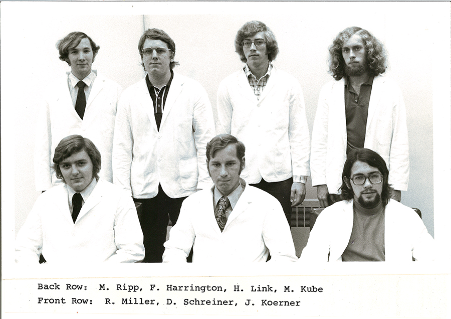A black-and-white group photo of pharmacy students in white coats.