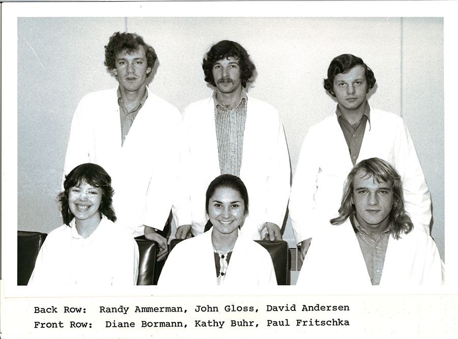 A black-and-white group photo of pharmacy students in white coats.