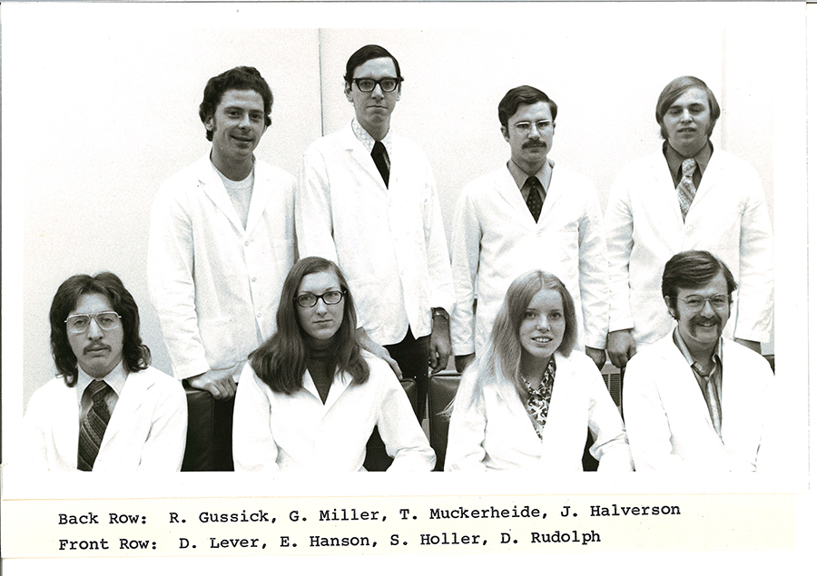 A black-and-white group photo of pharmacy students in white coats.