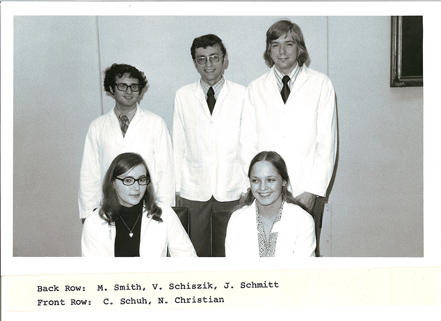 A black-and-white group photo of pharmacy students in white coats.