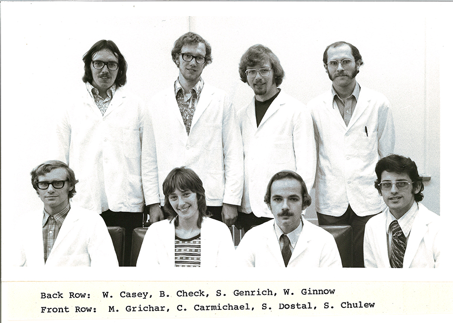 A black-and-white group photo of pharmacy students in white coats.