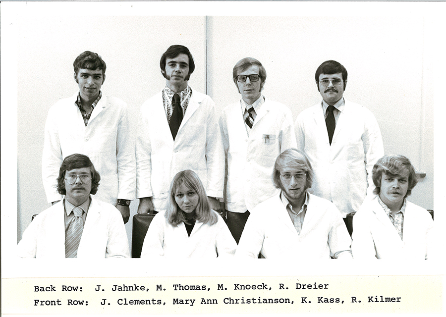 A black-and-white group photo of pharmacy students in white coats.