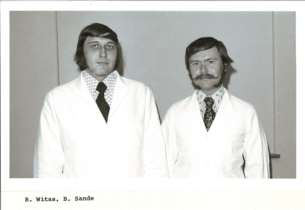 A black-and-white group photo of pharmacy students in white coats.