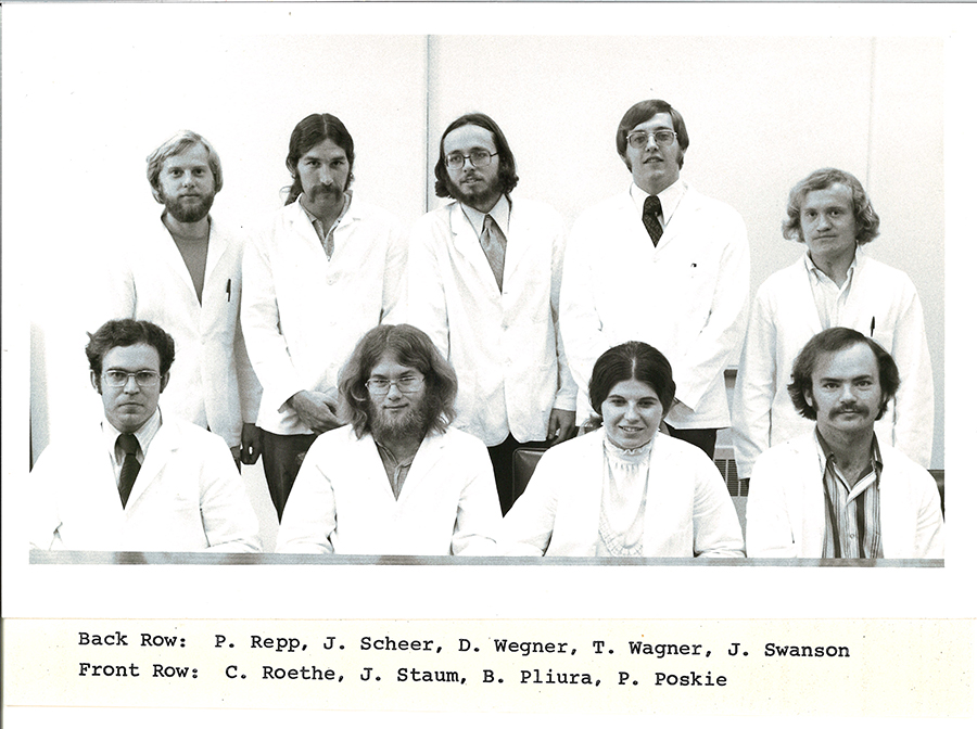A black-and-white group photo of pharmacy students in white coats.