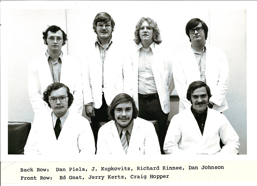 A black-and-white group photo of pharmacy students in white coats.