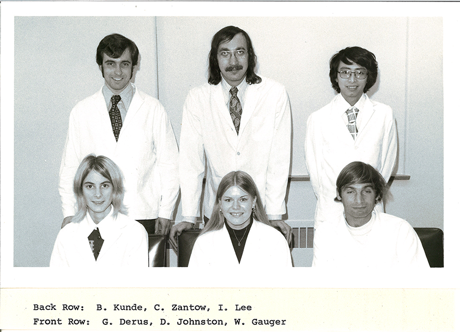 A black-and-white group photo of pharmacy students in white coats.