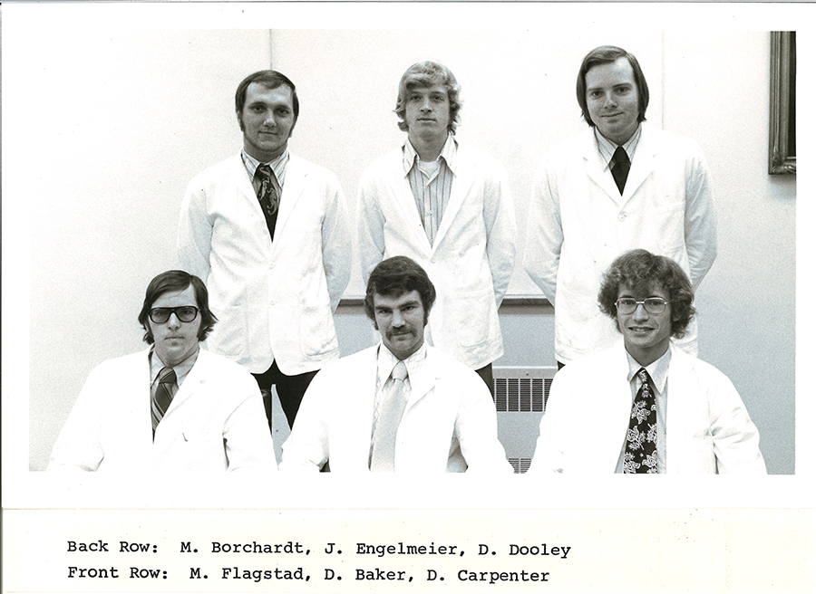 A black-and-white group photo of pharmacy students in white coats.