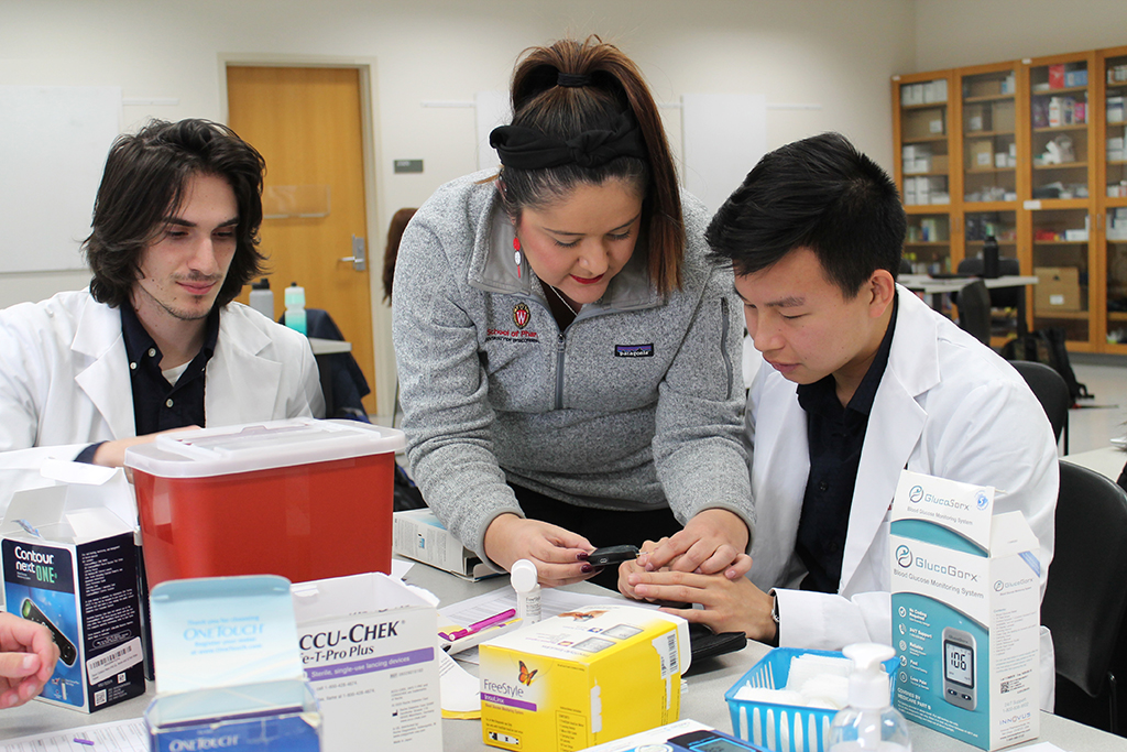 Marina Maes explains glucose monitors to PharmD students at a table