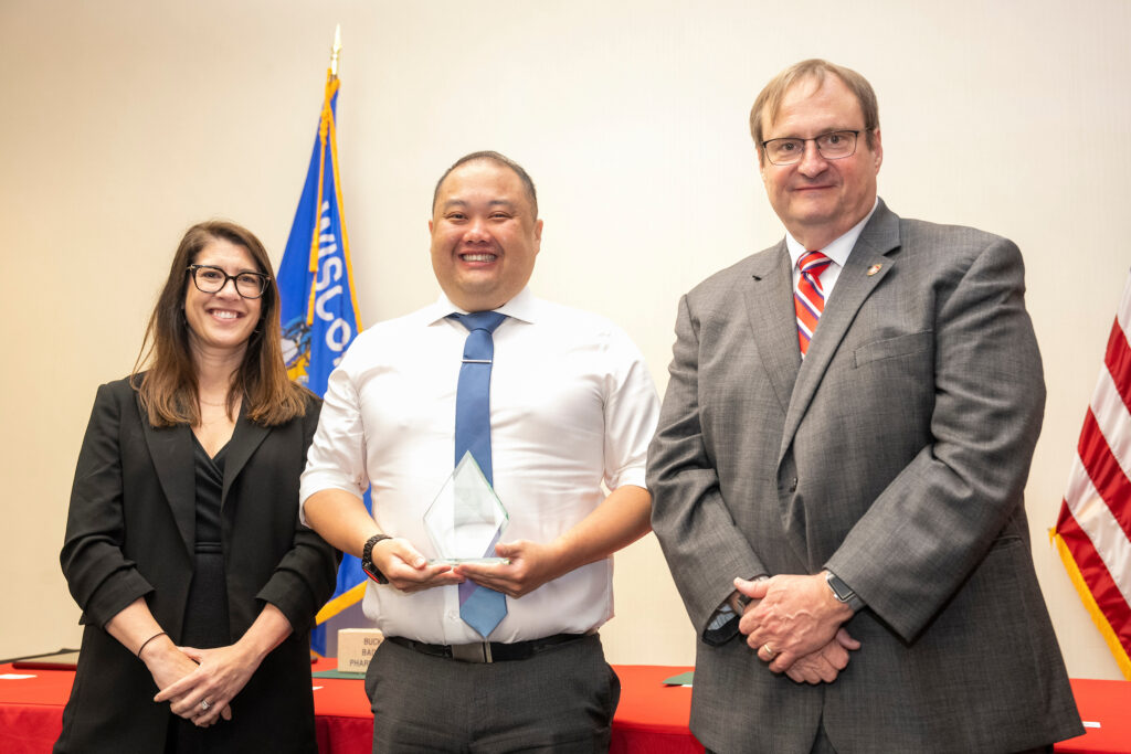 Mark Moua poses with an award, Dean Steve Swanson, and Lisa Imhoff.
