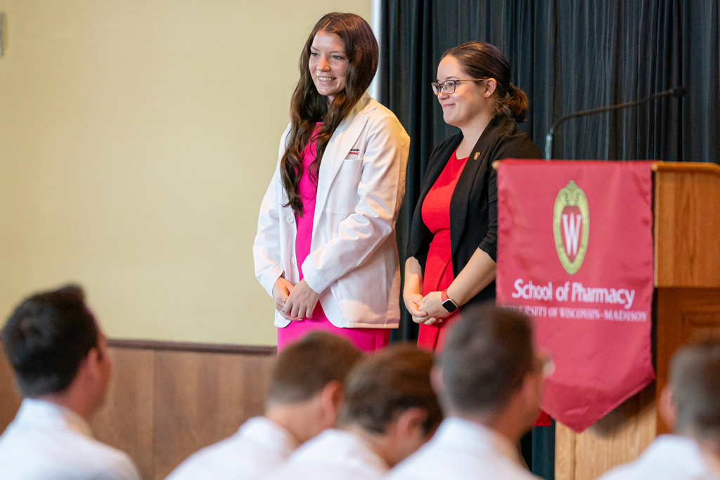 Student in white coat smiling with staff on-stage