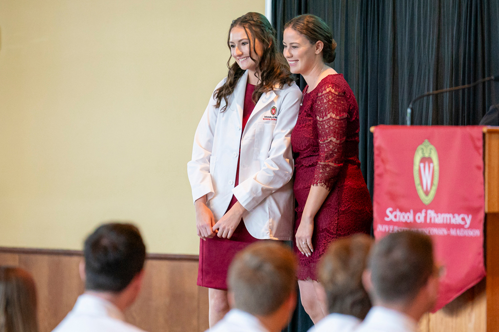 Student in white coat smiling with staff on-stage