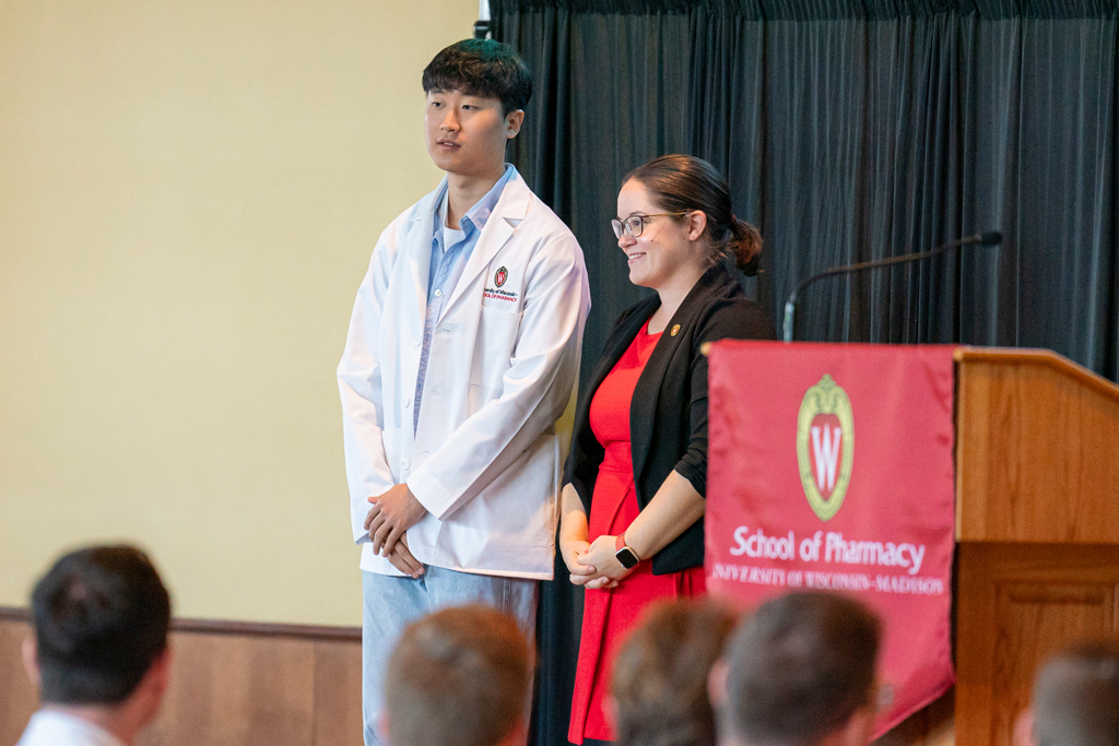 Student in white coat smiling with staff on-stage