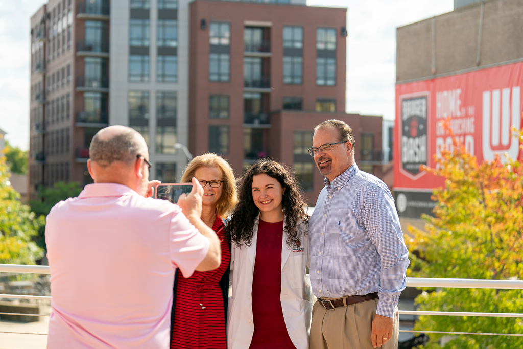 Student in white coat smiling with her family outside