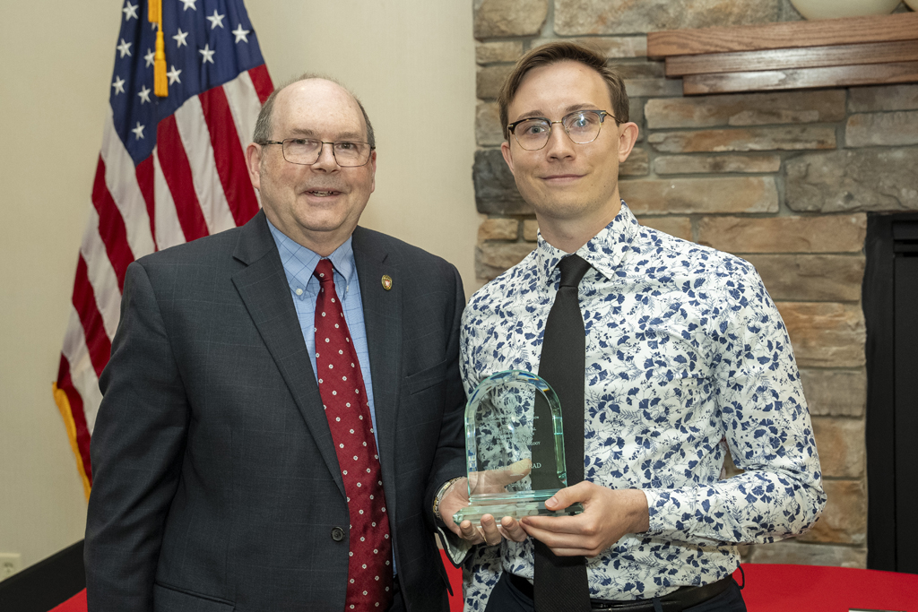 A graduate poses with Ed Elder and an award
