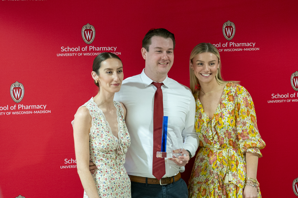 A graduate poses with an award and two guests