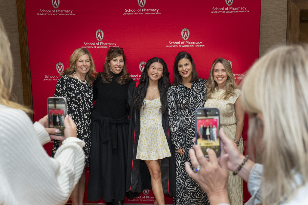 A graduate poses with family members in front of a red School of Pharmacy background