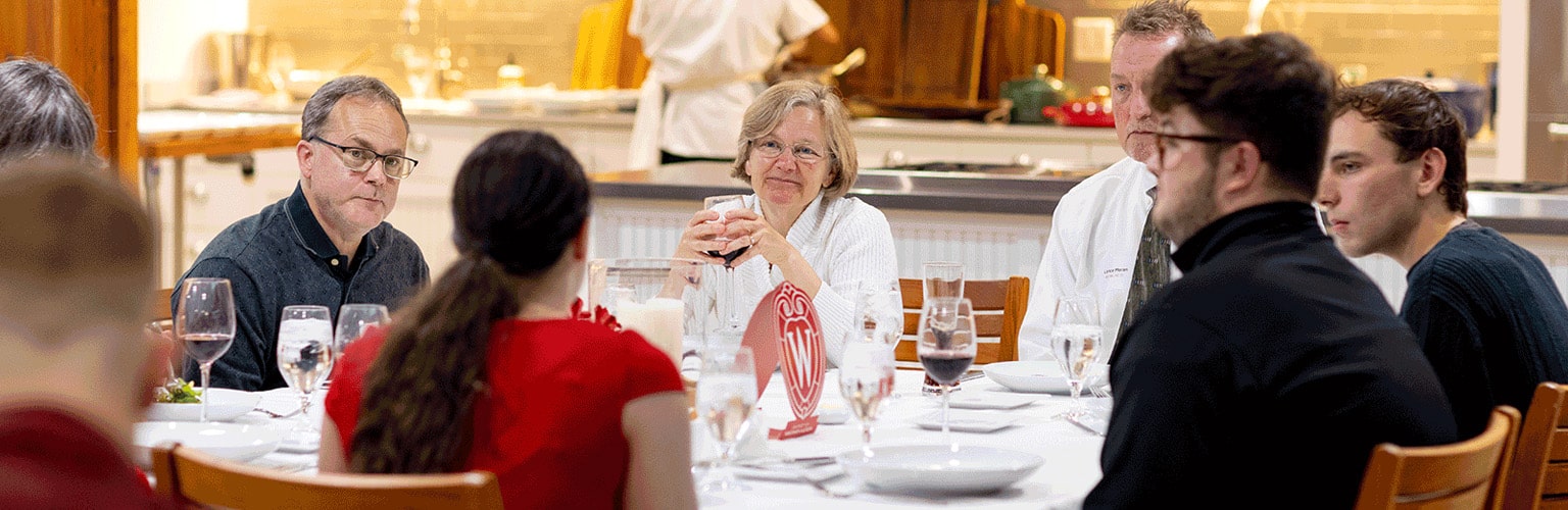 a group of six seated at a table converses at a School of Pharmacy alumni event