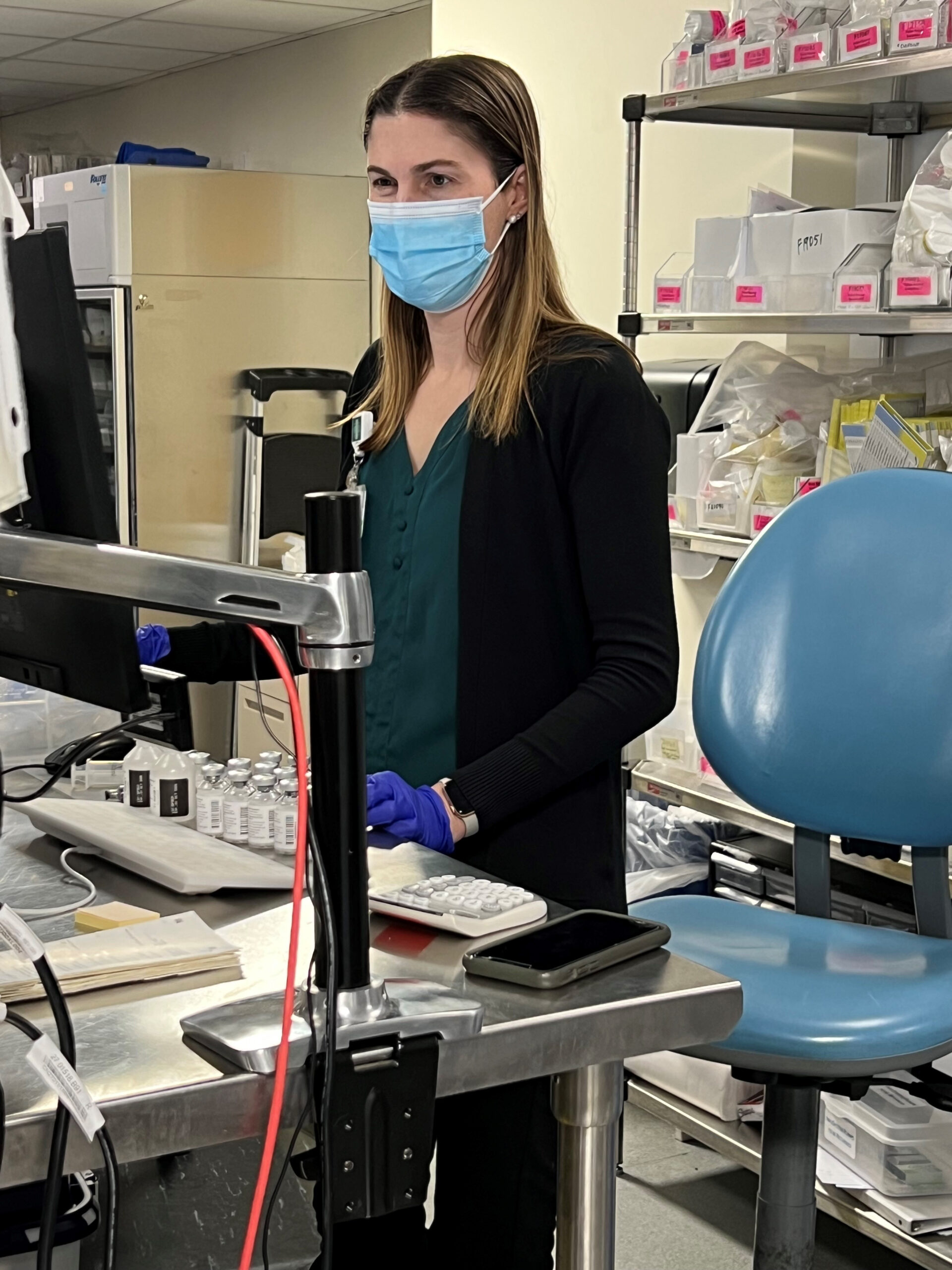 Andrea Gray working with a mask and gloves on at a computer.