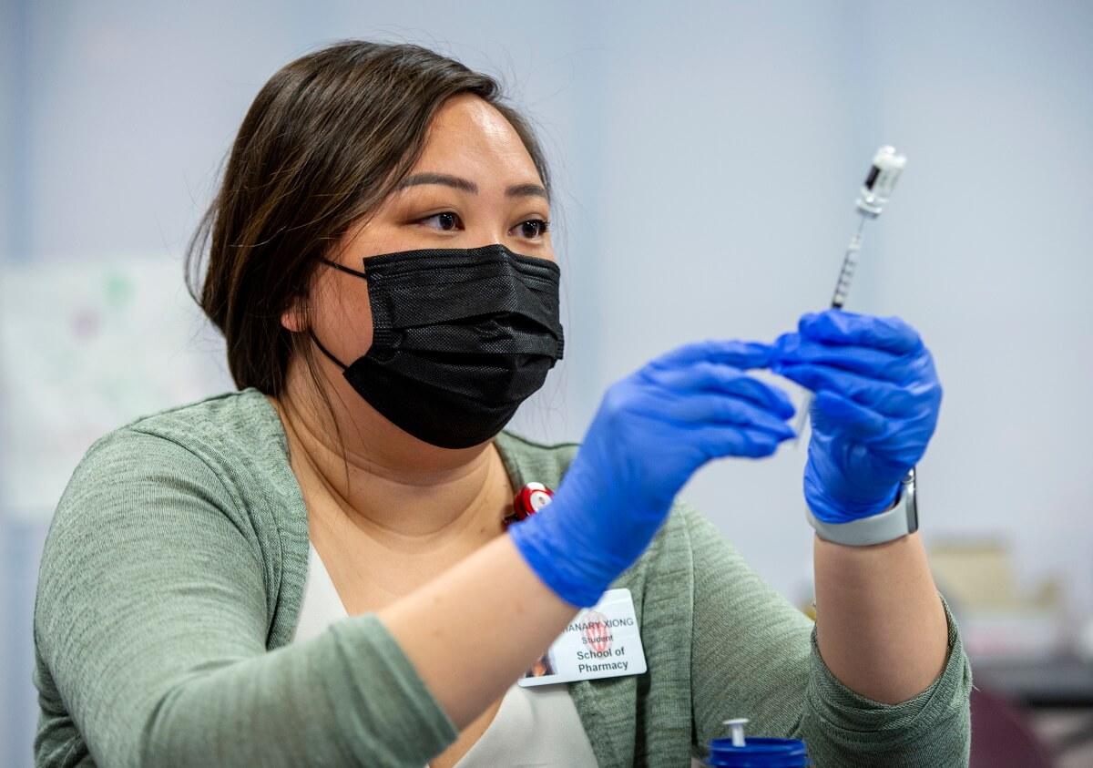 Phanary Xiong, wearing a mask and blue gloves, holds a vaccine needle