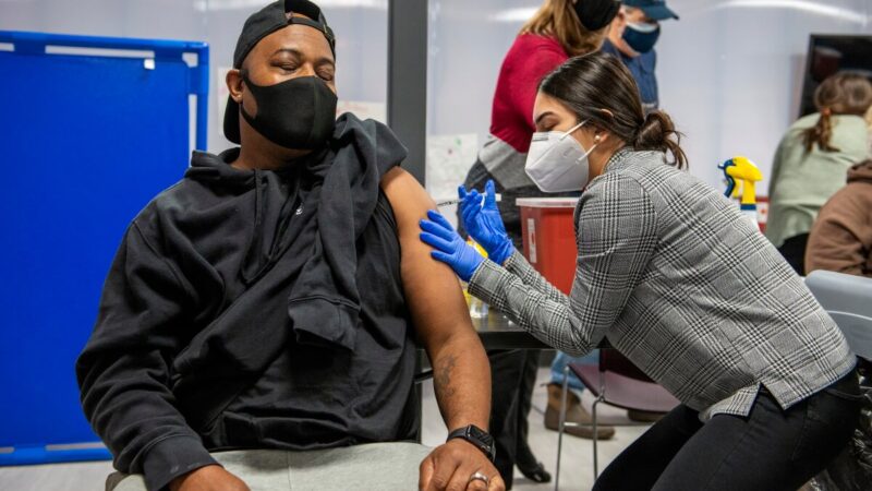 PharmD student Mahnoor Khan administers a vaccine to a patient in a black shirt.