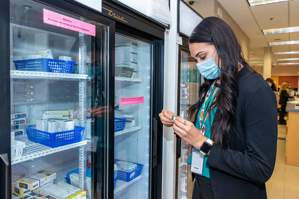 Kymberly Ludwig reviewing a medication near a refrigeration unit