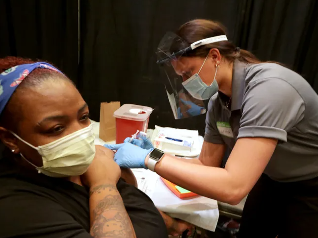 Volunteer wearing face shield and mask delivering covid vaccine to patient