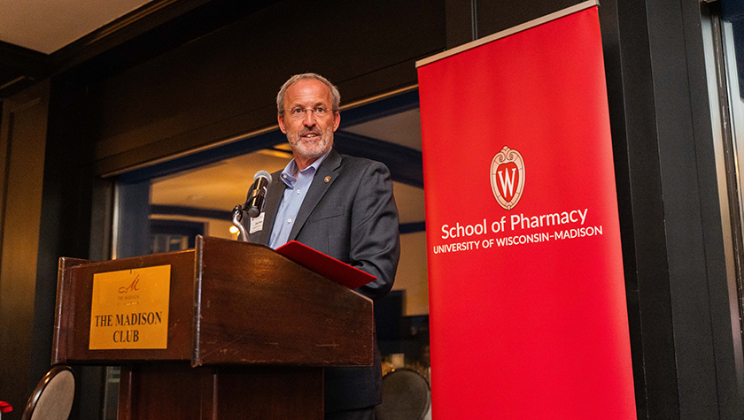 Dave Mott speaks at a lectern in front of a red School of Pharmacy banner