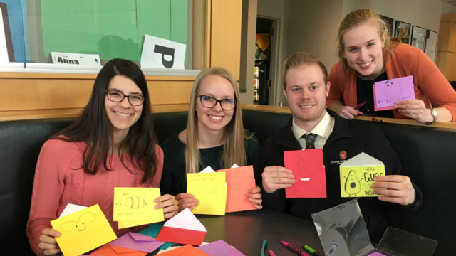 Lindsey Skubitz, Kelsey Eickstaedt, Bernard Brooks, and Olivia Merillat holding up colorful valentine's cards with paper and markers in front of them.