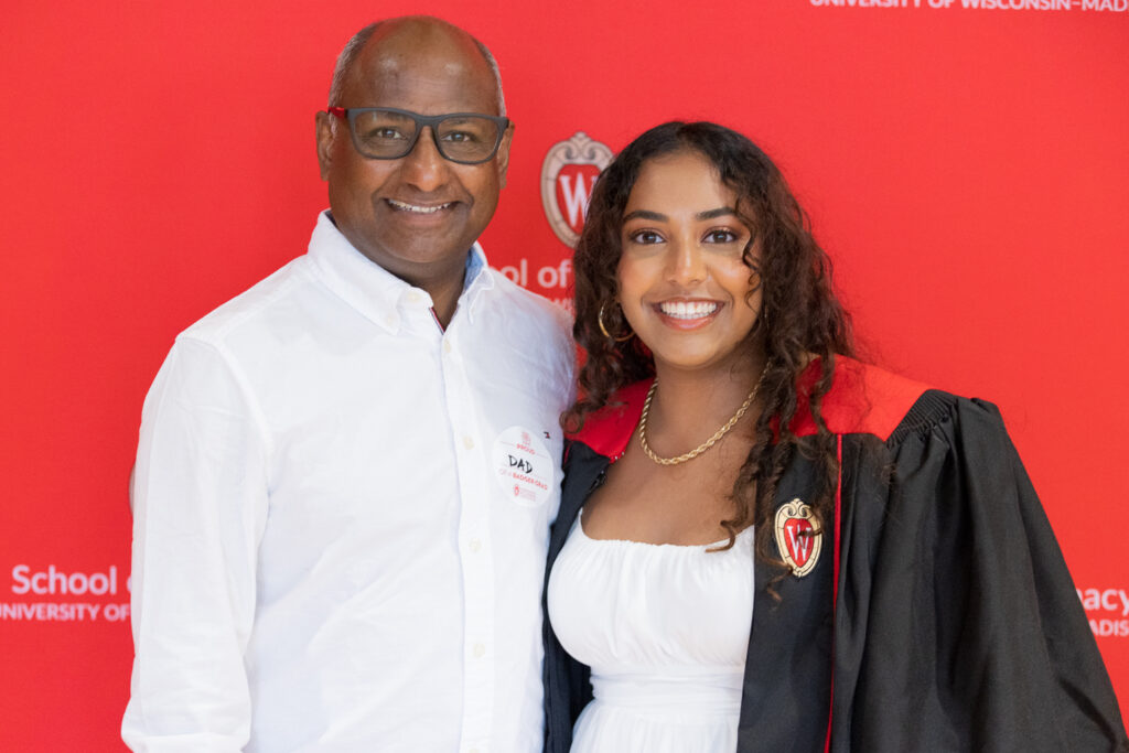 A PharmTox graduate and her family pose in front of the red School of Pharmacy backdrop.
