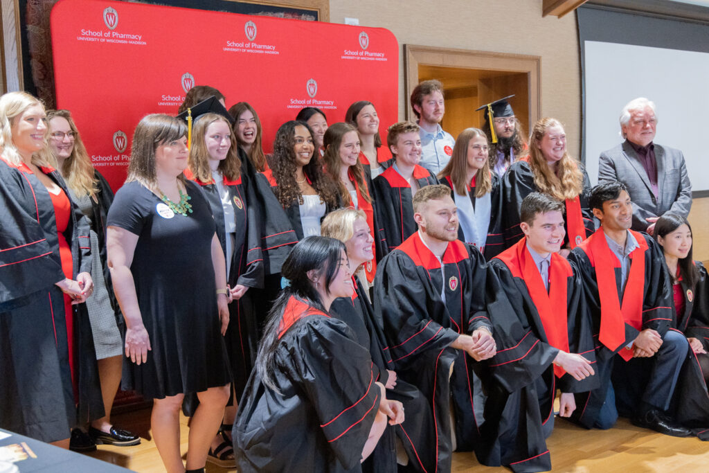 The 2023 PharmTox class poses in front of the red School of Pharmacy background.