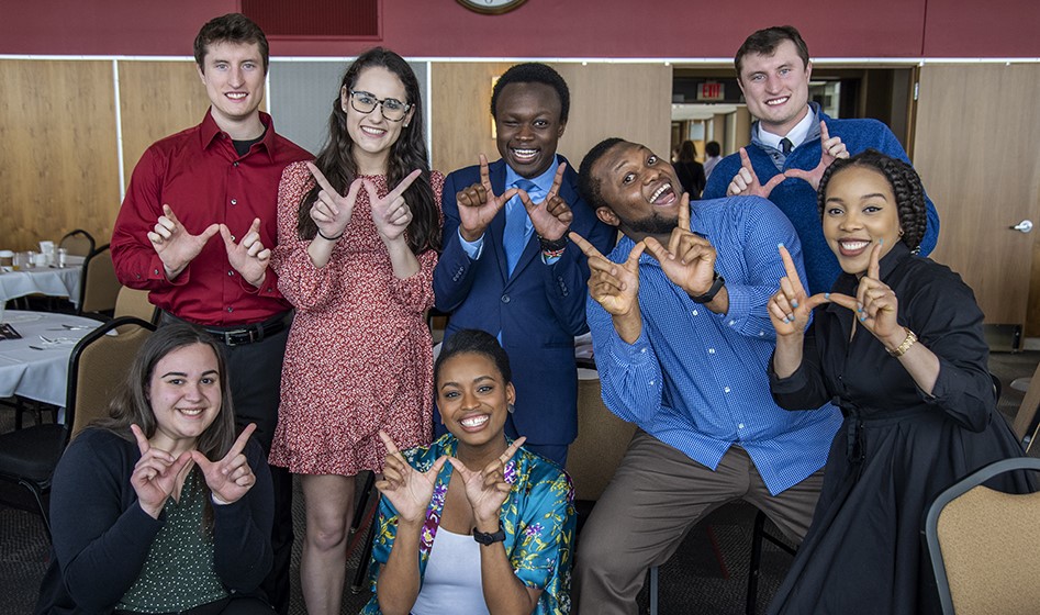 Students together in a large dining room, using their hands to form a "W" for the camera