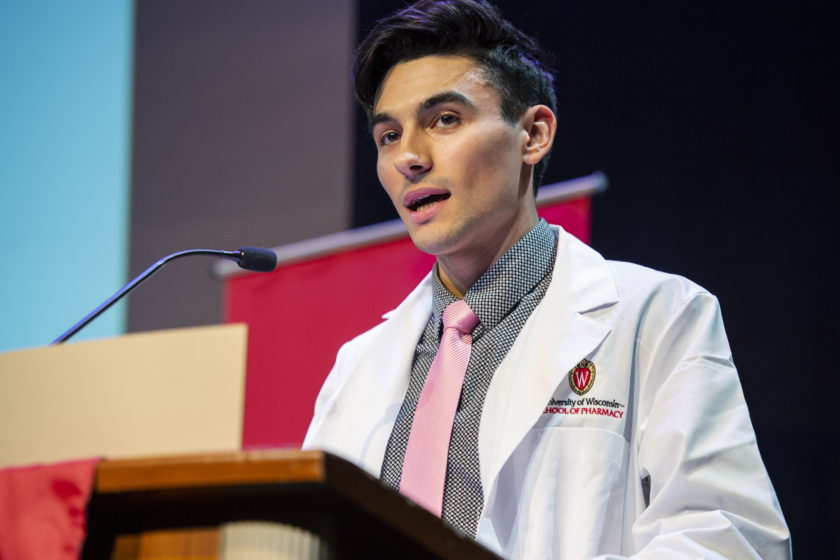 Student in white coat speaking at podium during white coat ceremony