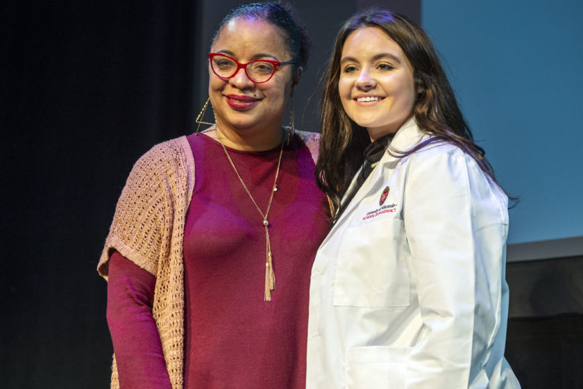 Student wearing white coat taking picture with staff during white coat ceremony