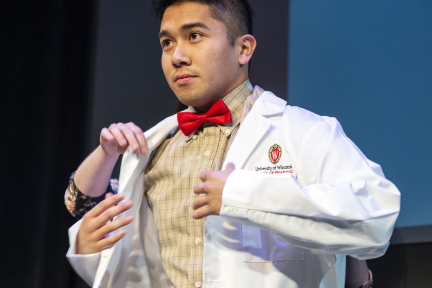 Staff helping student put on white coat during white coat ceremony