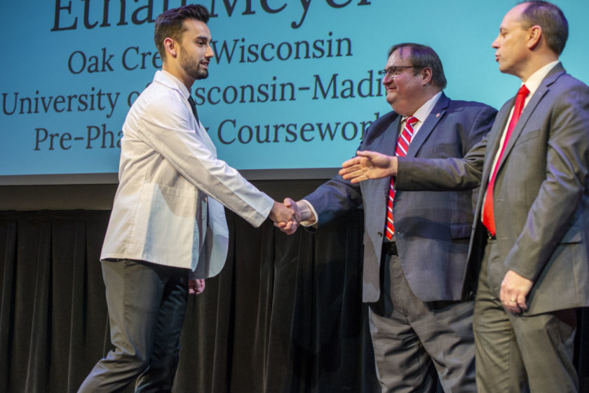 Student in white coat shaking hands with Steve Swanson during white coat ceremony