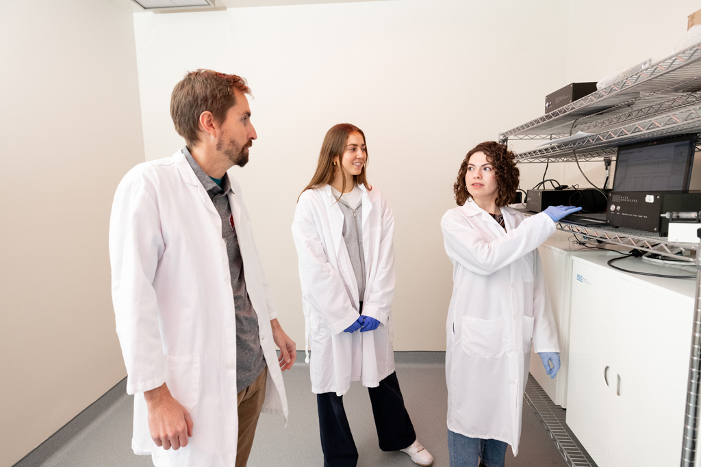 Wenthur talks with Nicole Stigler (middle), an undergraduate research assistant, and Natalie González Velázquez, a graduate student in the Pharmaceutical Sciences PhD Program, as they look at operant conditioning boxes used to study rat behavior. 