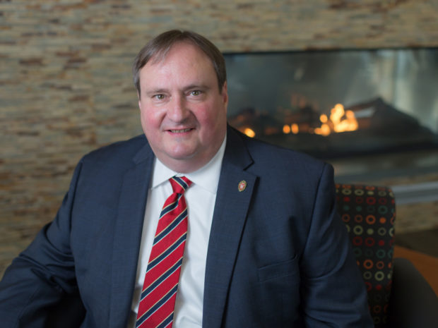 Dean Steve Swanson sits next to a cosy fireplace