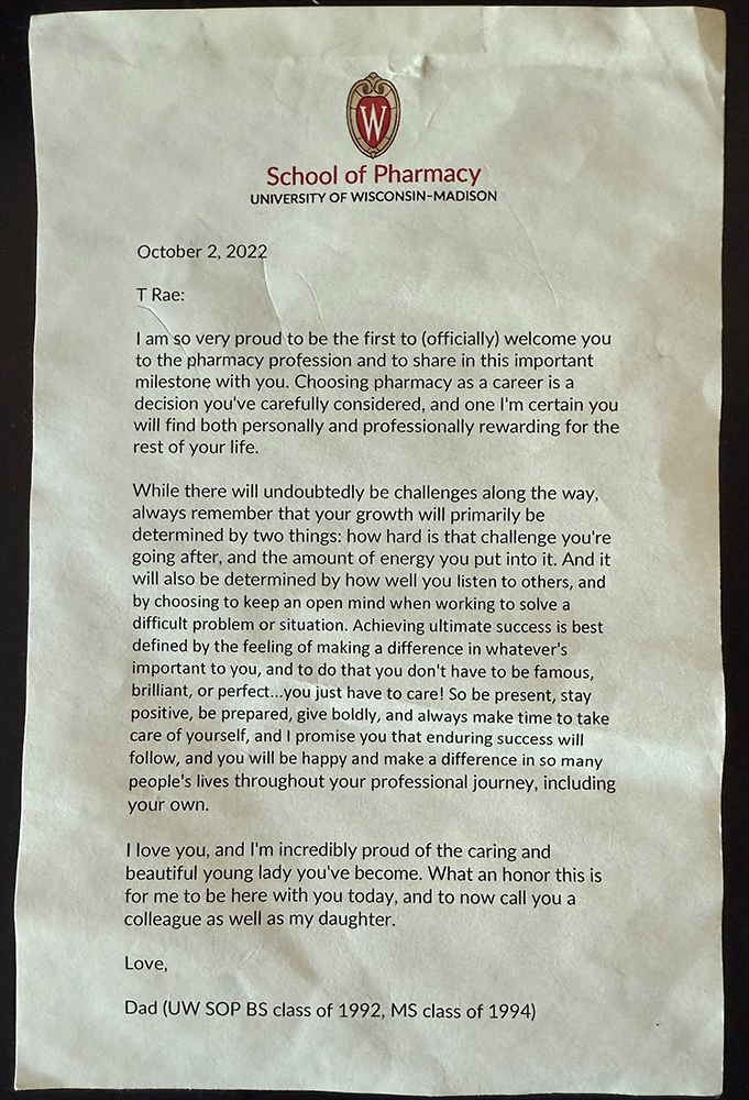 An image of a letter that reads as follows:

School of Pharmacy University of Wisconsin-Madison

October 2, 2022

T Rae:

I am so very proud to be the first to (officially) welcome you to the pharmacy profession and to share in this important milestone with you. Choosing pharmacy as a career is a decision you've carefully considered, and one I'm certain you will find both personally and professionally rewarding for the rest of your life.

While there will undoubtedly be challenges along the way, always remember that your growth will primarily be determined by two things: how hard is that challenge you're going after, and the amount of energy you put into it. And it will also be determined by how well you listen to others, and by choosing to keep an open mind when working to solve a difficult problem or situation. Achieving ultimate success is best defined by the feeling of making a difference in whatever's important to you, and to do that you don't have to be famous, brilliant, or perfect...you just have to care! So be present, stay positive, be prepared, give boldly, and always make time to take care of yourself, and I promise you that enduring success will follow, and you will be happy and make a difference in so many people's lives throughout your professional journey, including your own.

I love you, and I'm incredibly proud of the caring and beautiful young lady you've become. What an honor this is for me to be here with you today, and to now call you a colleague as well as my daughter.

Love,

Dad (UW SOP BS class of 1992, MS class of 1994)
