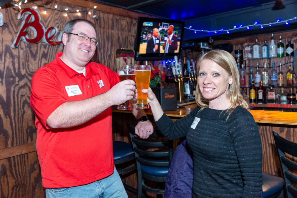 Ryan Miller and Tanya Hall toasting beer glasses together in front of a bar