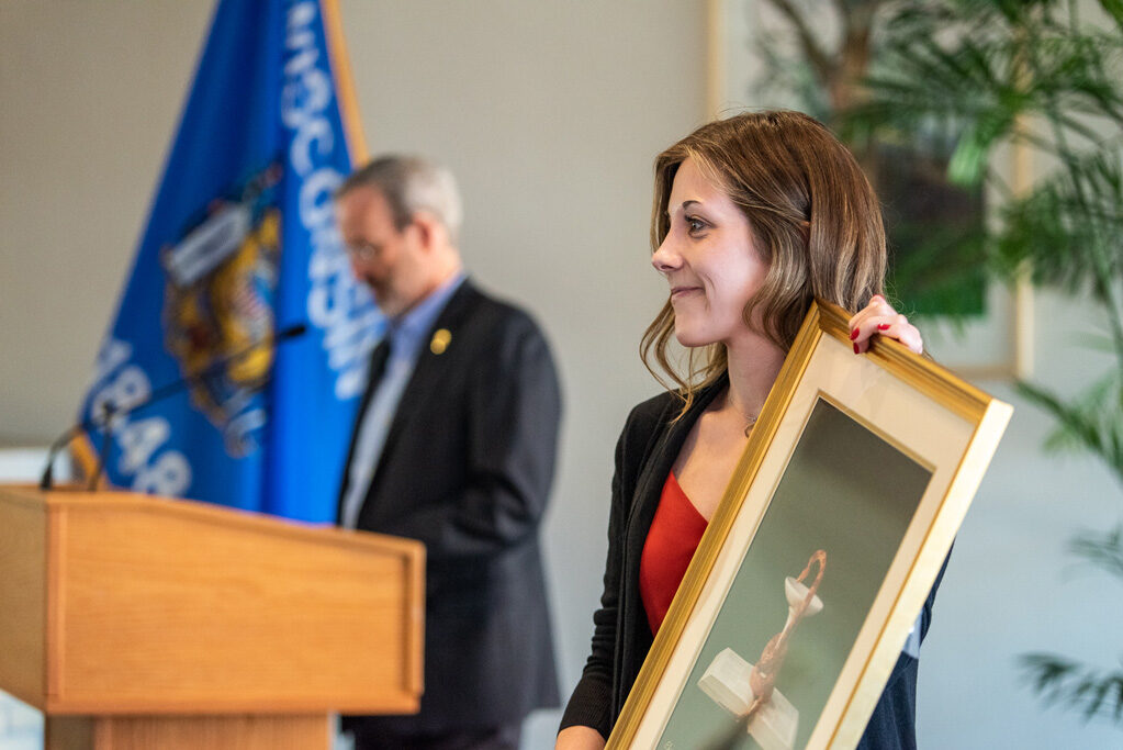 Graduate student holding up painting with Dave Mott at podium in background